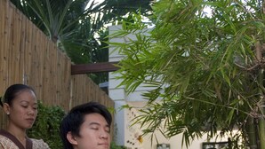 A person receiving a massage in a serene outdoor setting with a wooden fence and greenery. - Nantra De Boutique (Pattaya)