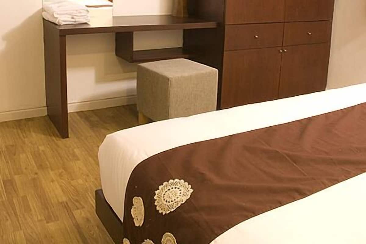 Une chambre d’hôtel avec un lit, une table de chevet, une armoire en bois et un petit tabouret.