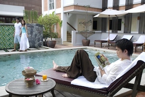 Ein Poolbereich mit Liegestühlen, einem Tisch mit Getränken und Snacks sowie einer Person, die ein Buch liest.