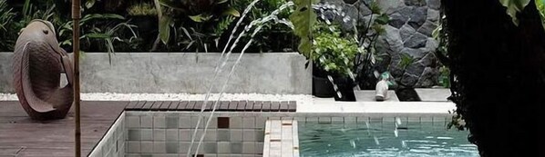 Ein Pool mit Fliesenrand, umgeben von einer Steinmauer und Grünpflanzen.