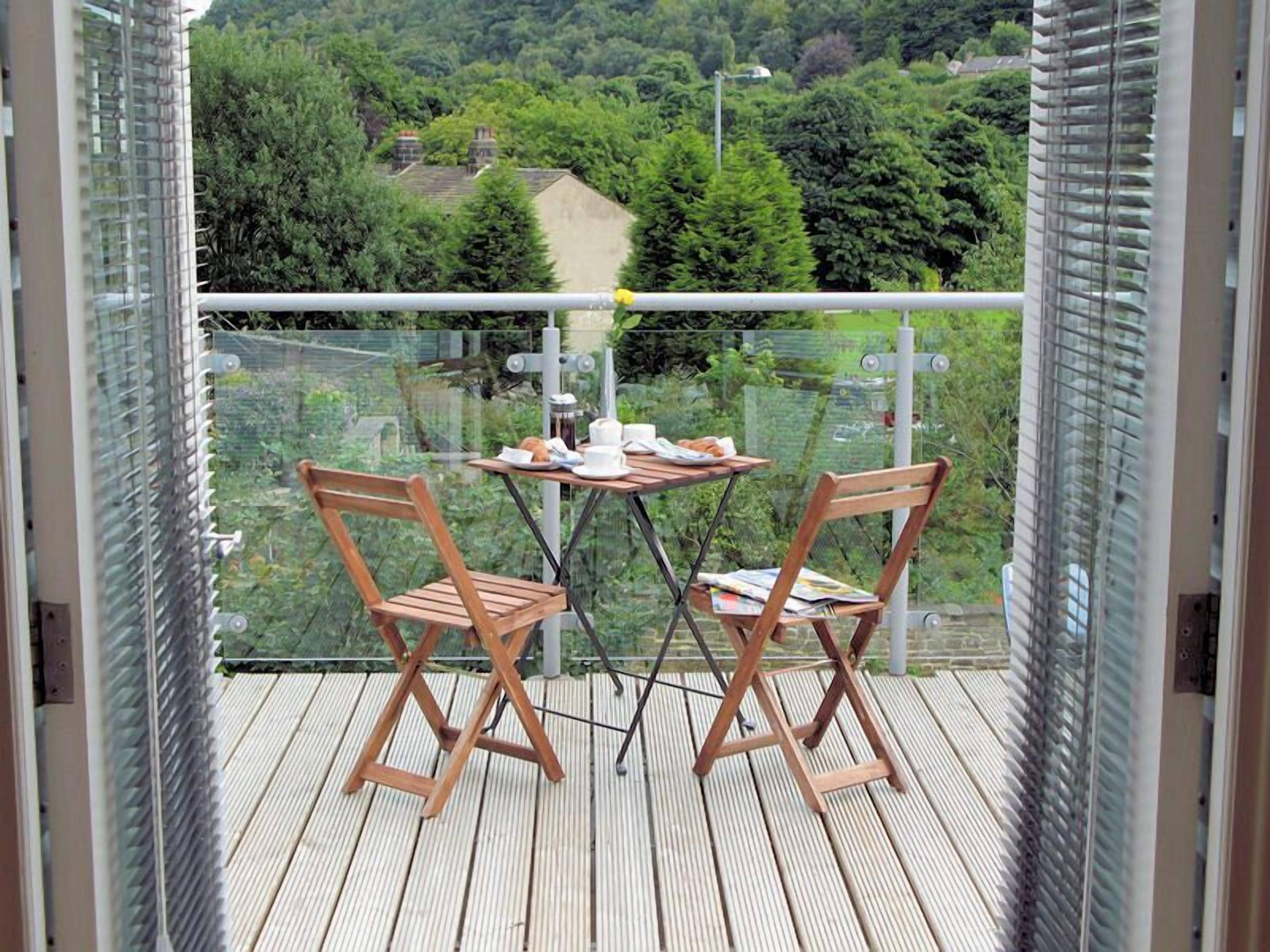 A balcony with two wooden chairs and a small table, overlooking a lush green landscape.