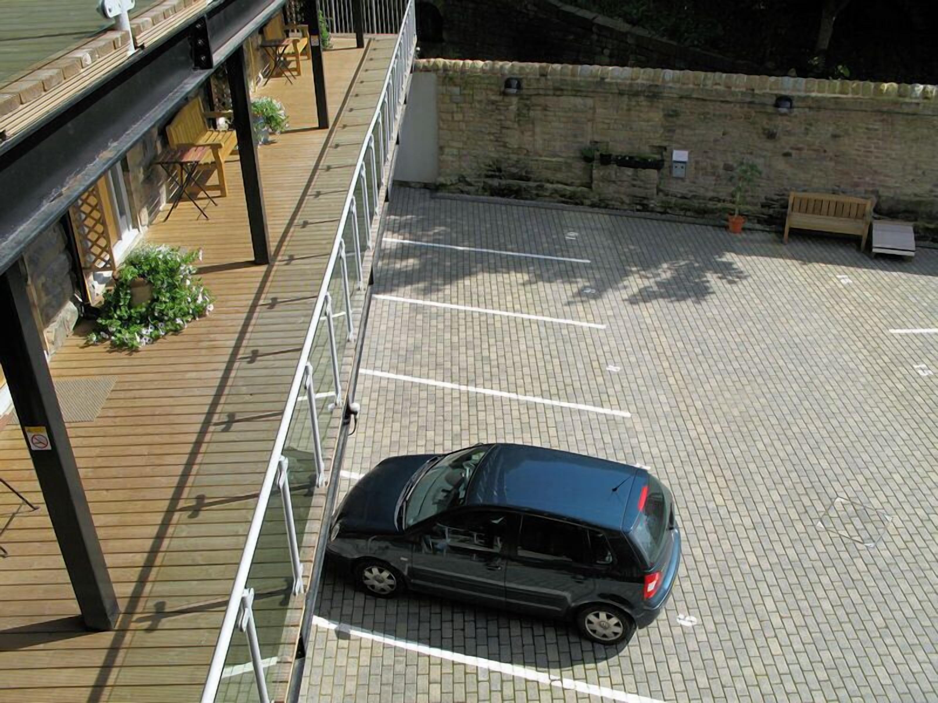 A parking area with a car, a wooden deck, and a stone wall.
