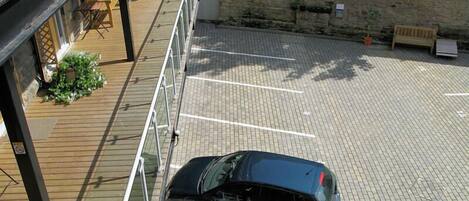 A parking area with a car, a wooden deck, and a stone wall.