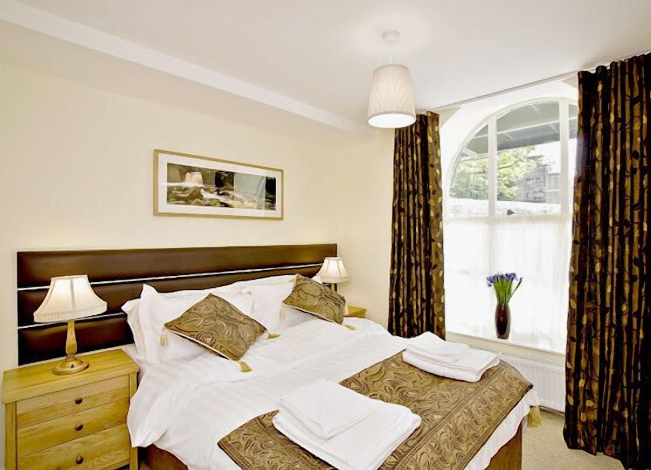 A hotel room with a large bed, two bedside tables, a nightstand, a window with curtains, and a wall-mounted picture.