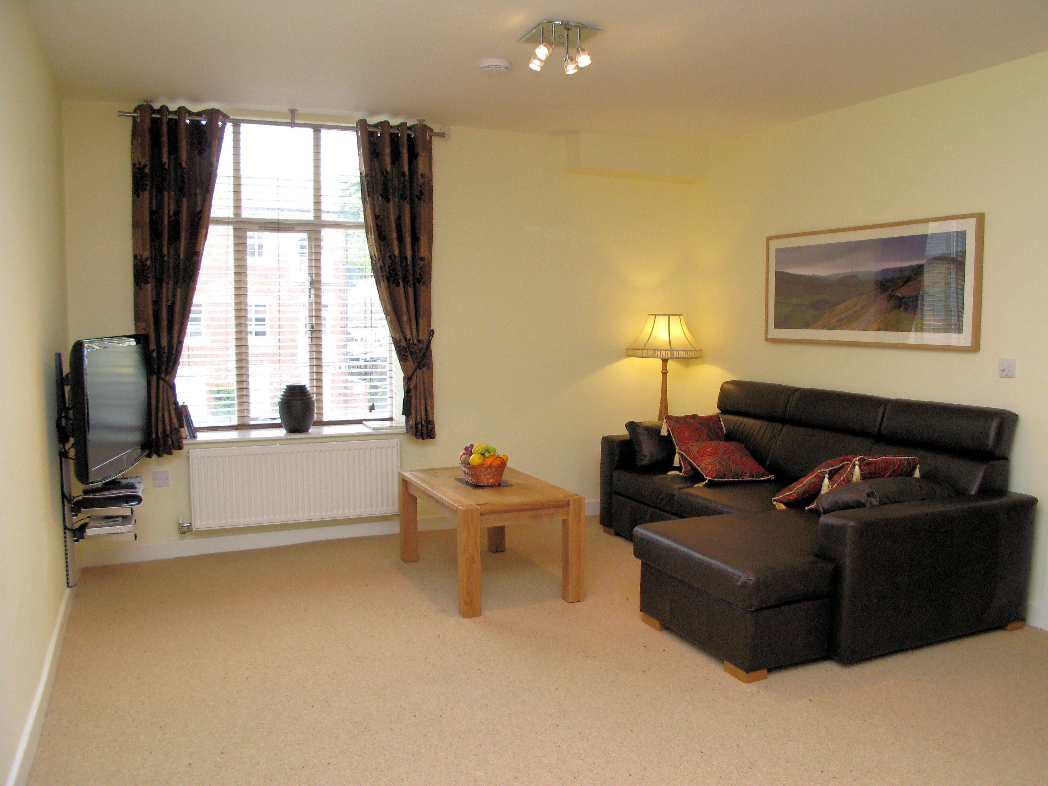 A living room with a sofa, a small table, a lamp, a television, and a window with curtains.