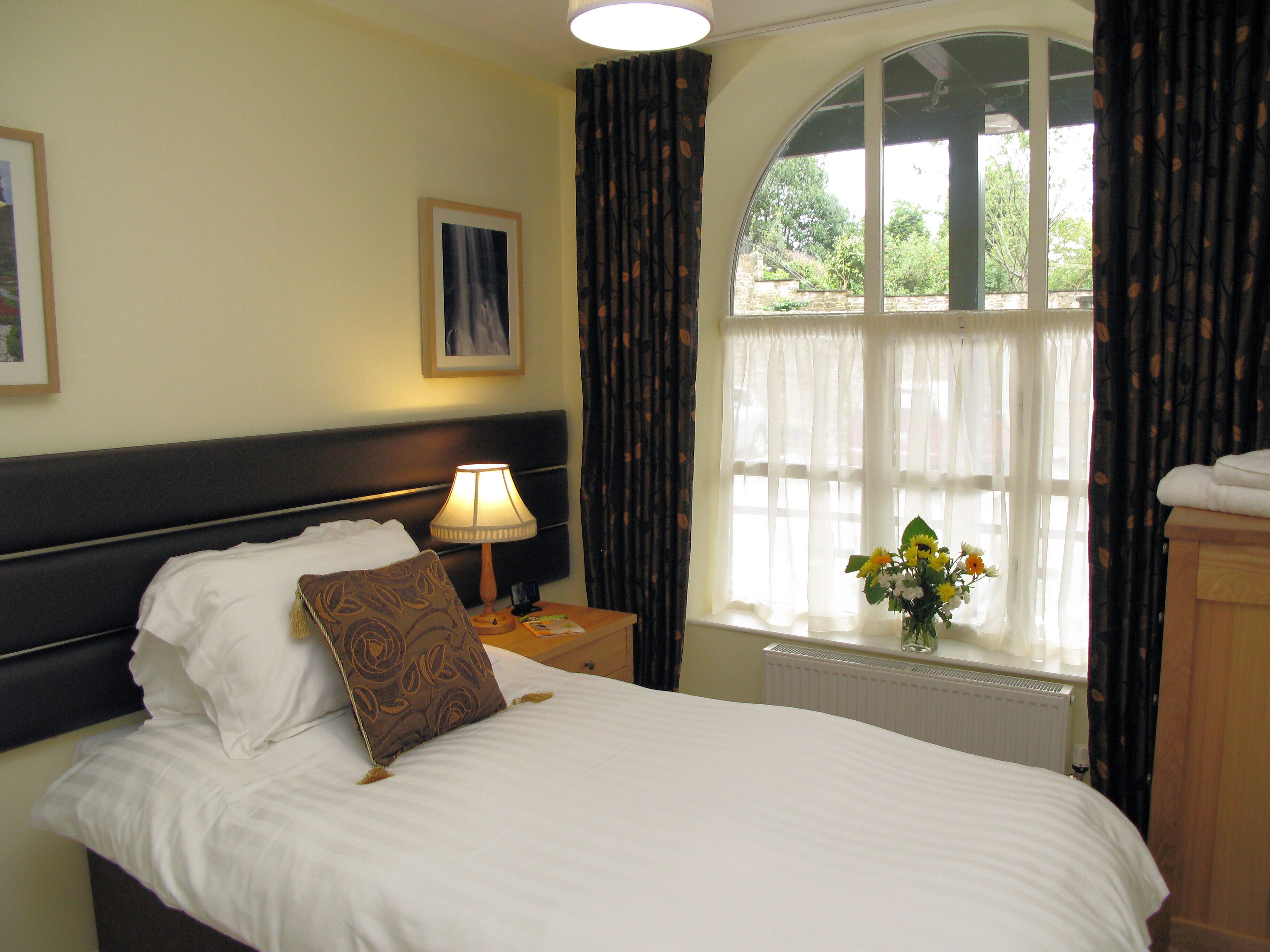 A neatly made bed with a pillow, a bedside lamp, a framed picture on the wall, and a window with curtains.