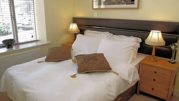 A neatly made bed with white linens and two decorative pillows, a bedside table with a lamp, and a framed artwork on the wall.