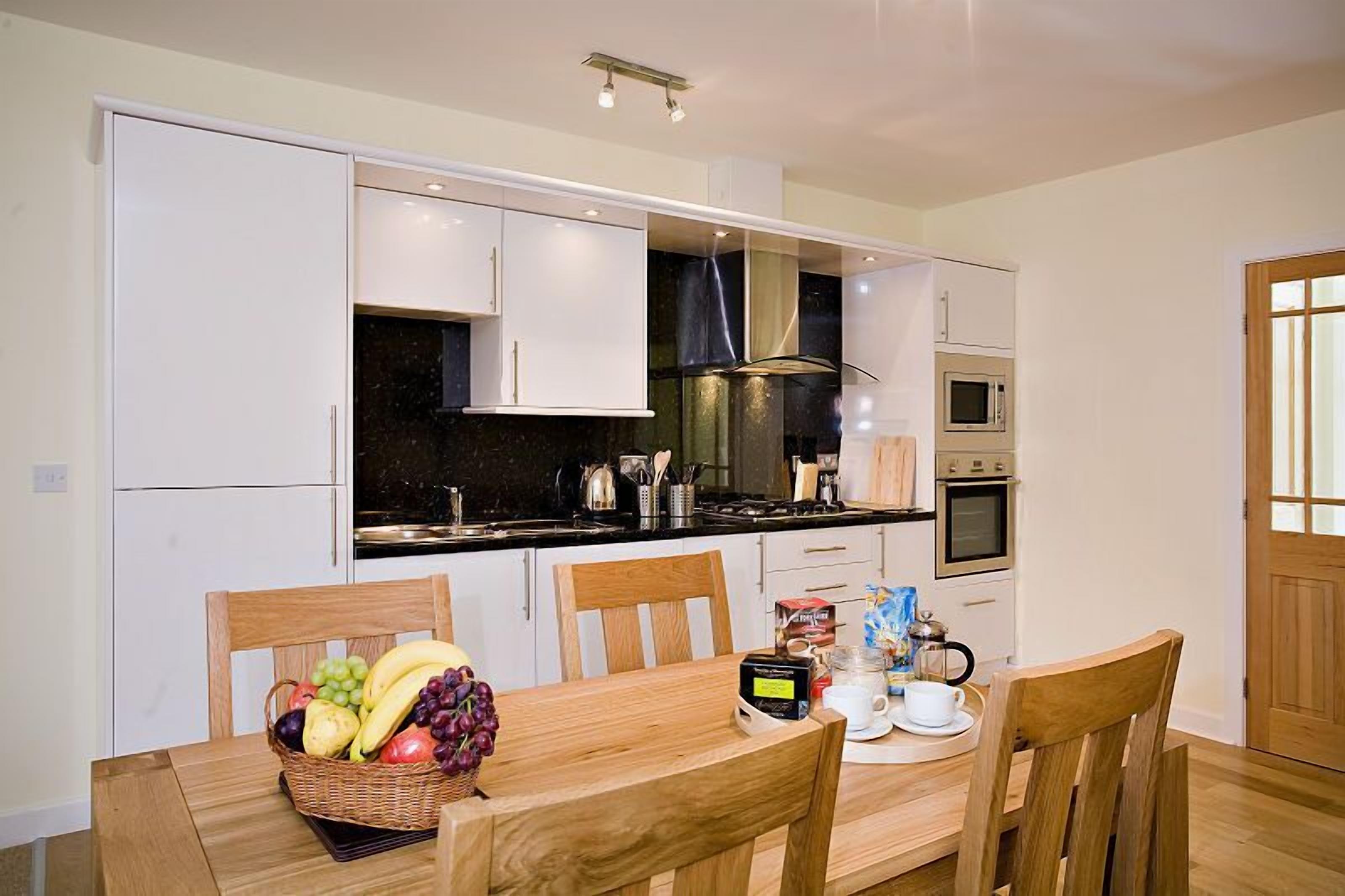 A modern kitchen with white cabinets, a black countertop, and a dining table with chairs.