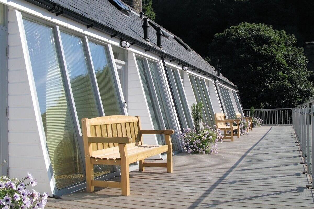 A row of rooms with large windows, a wooden bench, and a flower bed.