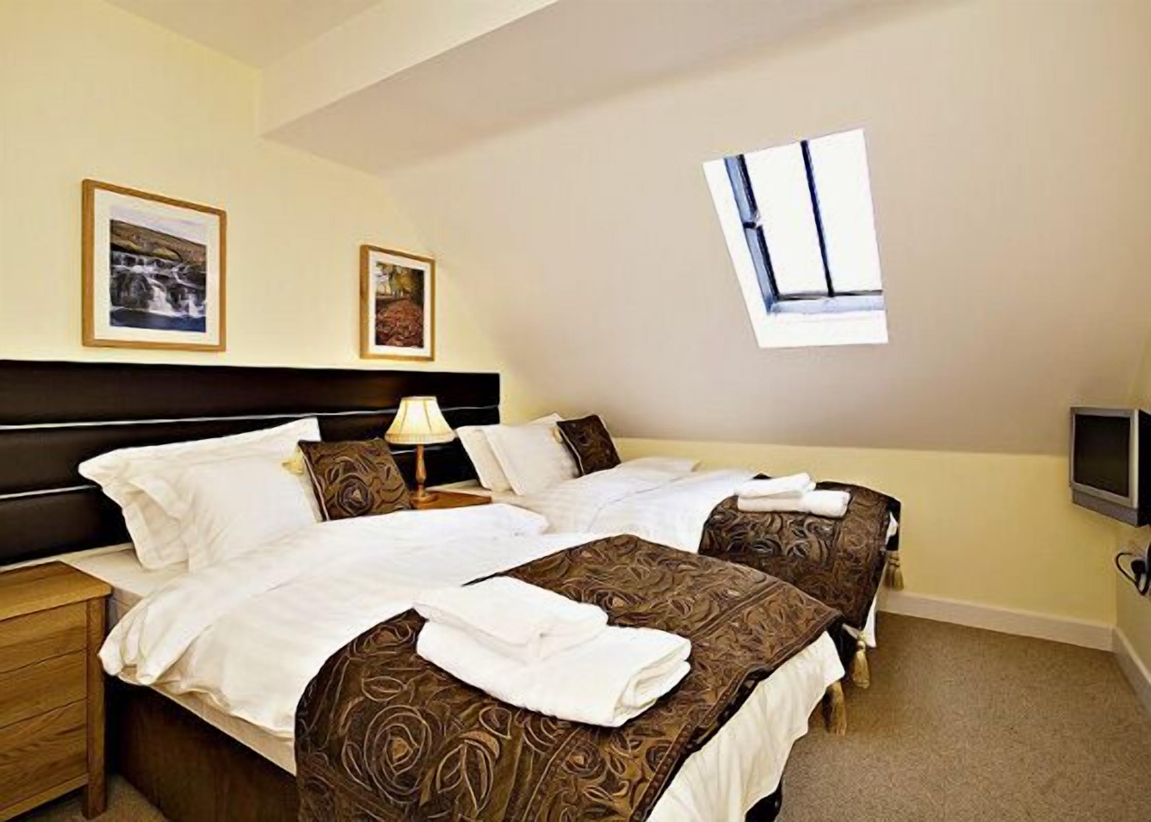 A hotel room with two beds, a nightstand, a lamp, a TV, and framed pictures on the wall.