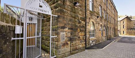 A stone building with a sign reading "TROF 1 - MELL APARTMENTS" and a gated entrance.