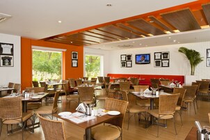 A spacious restaurant with high ceilings and natural light from large windows. Tables are set with white tablecloths and wicker chairs.
