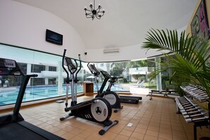 A gym with exercise equipment, a bench, and a large window overlooking a pool. - Lemon Tree Hotel, Ahmedabad (Ahmedabad)