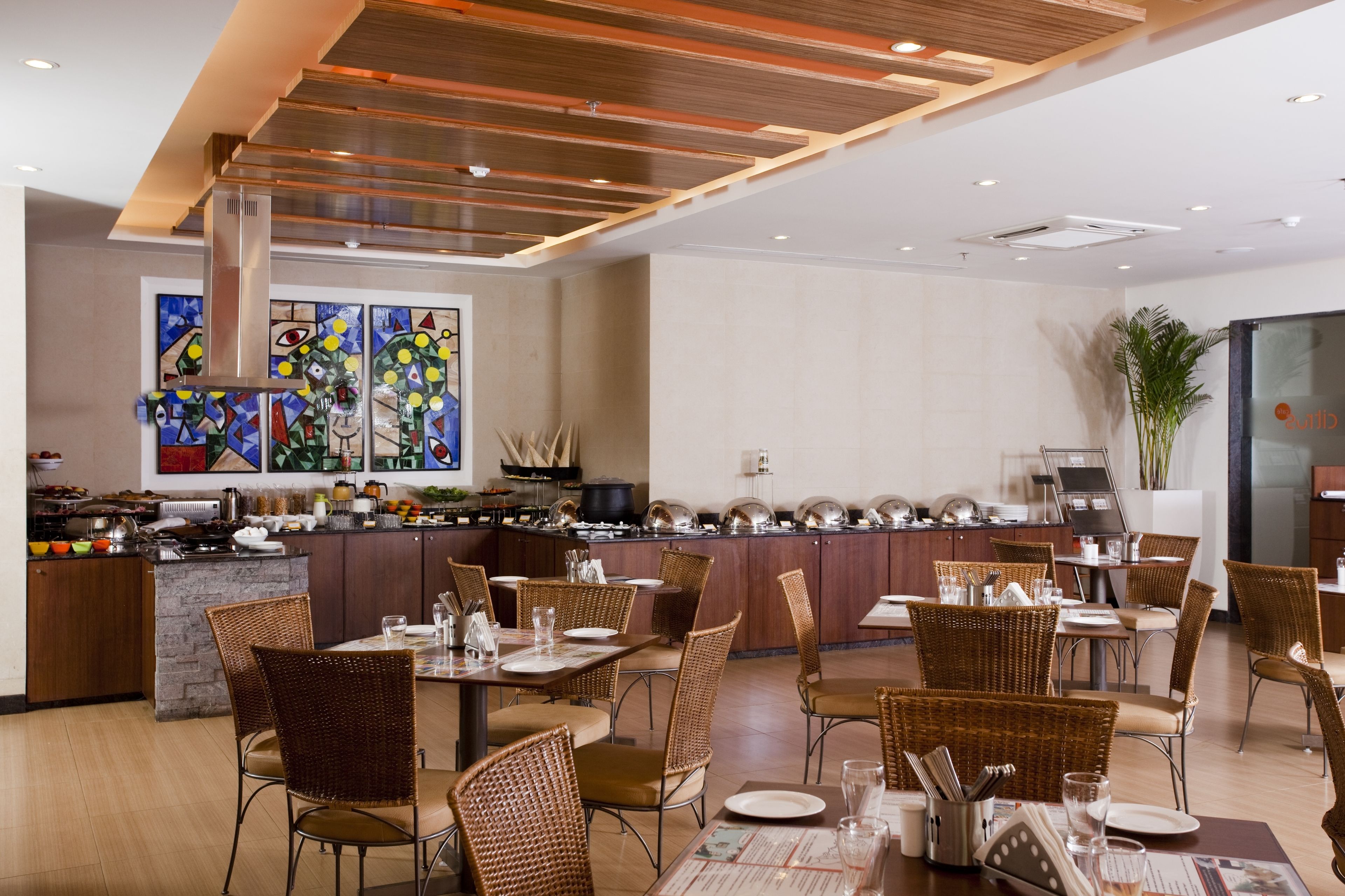 A modern restaurant with a central island, wicker chairs, and a variety of dining tables.
