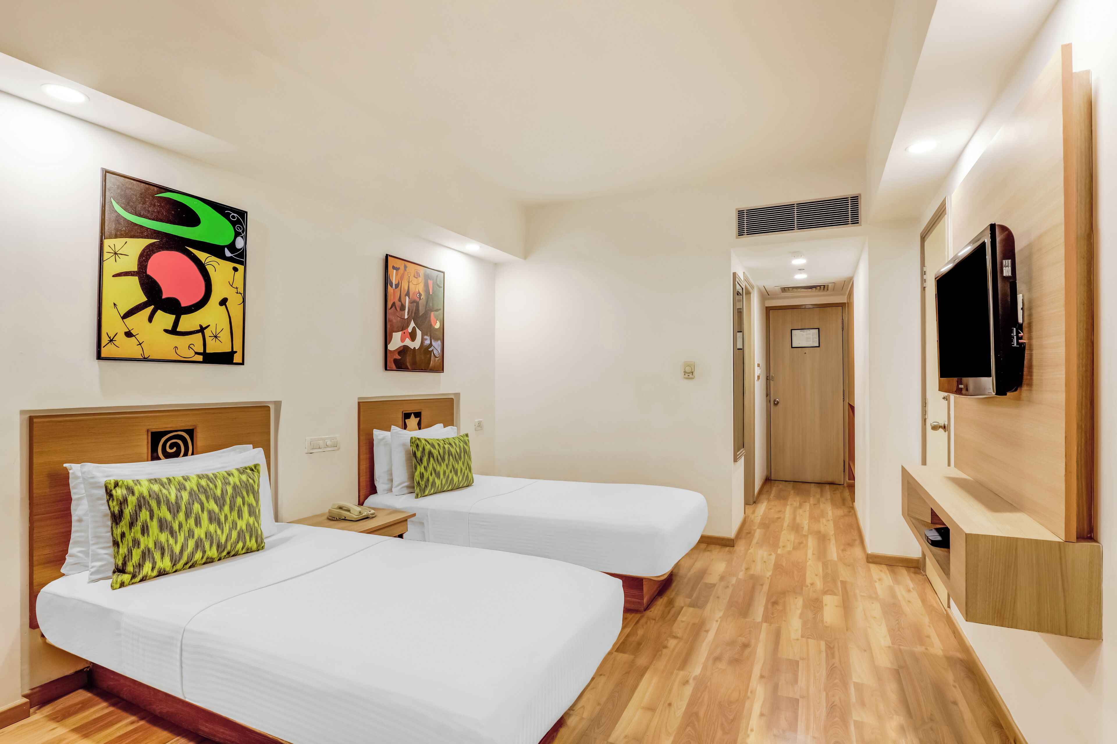 A hotel room with two beds, a TV, and artwork on the walls.