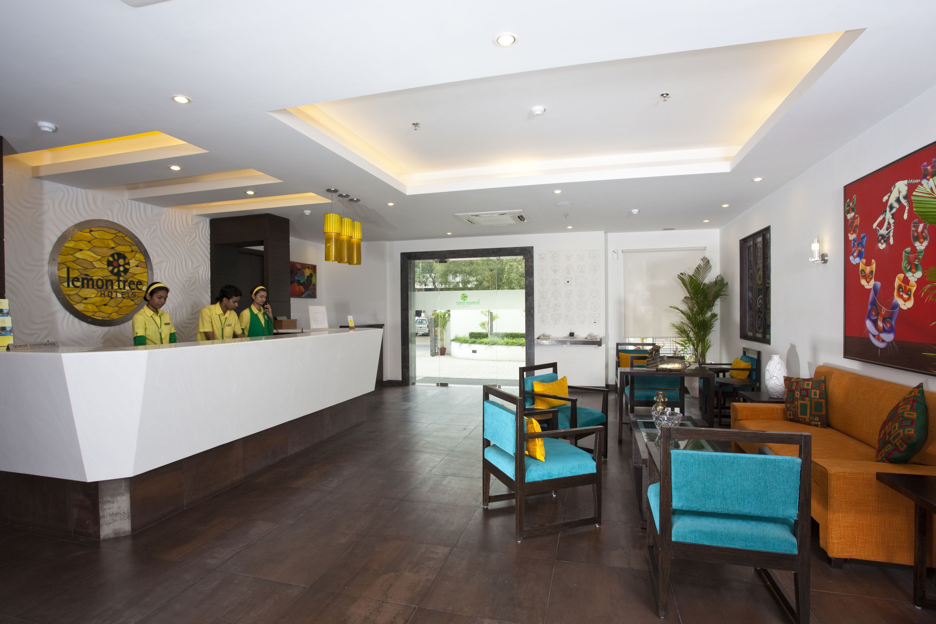 Un área de recepción de hotel con diseño moderno, que incluye un mostrador de recepción, zona de estar con sillas y sofás, y un ventanal con vistas al exterior.
