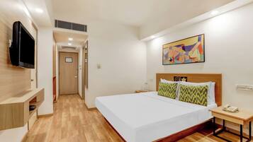A hotel room with a large bed, a bedside table with a phone, a TV mounted on the wall, and a colorful abstract painting above the bed.
