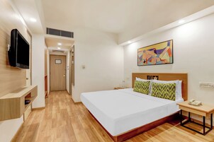 Quarto de hotel com uma cama grande, mesa de cabeceira com telefone, televisão na parede e uma pintura abstrata colorida acima da cama.