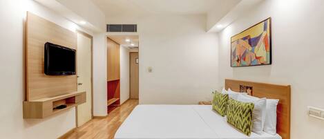 A hotel room with a bed, a bedside table with a telephone, a mounted television, and a painting on the wall.