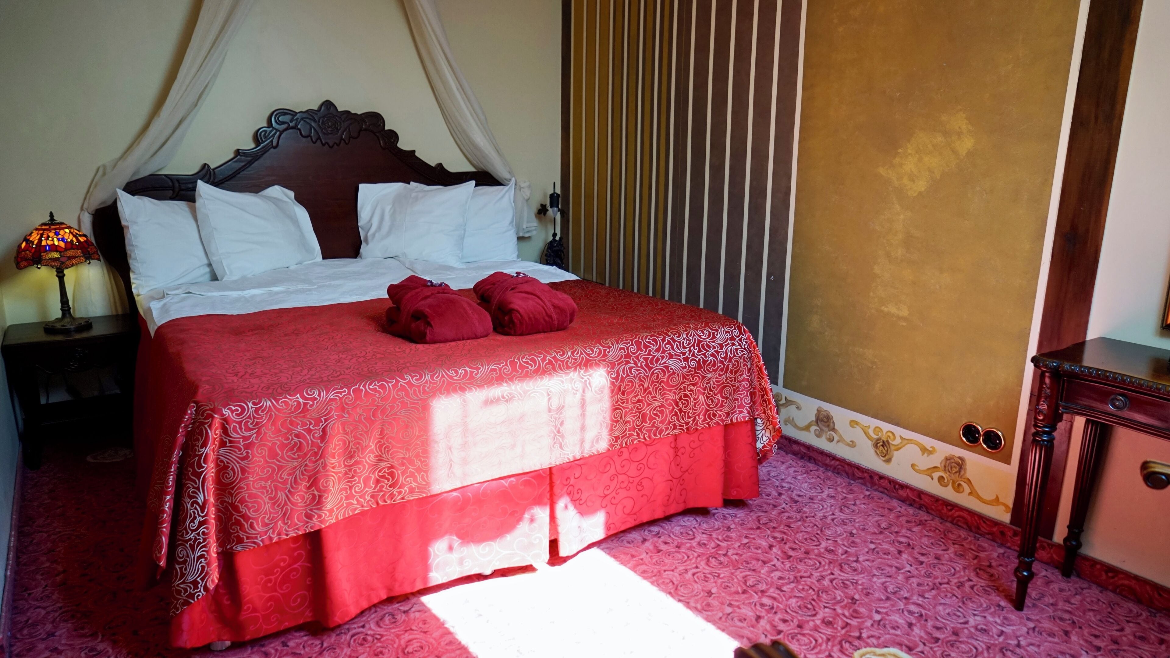 Un lit bien fait, avec une couverture rouge, des oreillers blancs et un plaid rouge posé sur un tapis à motifs.
