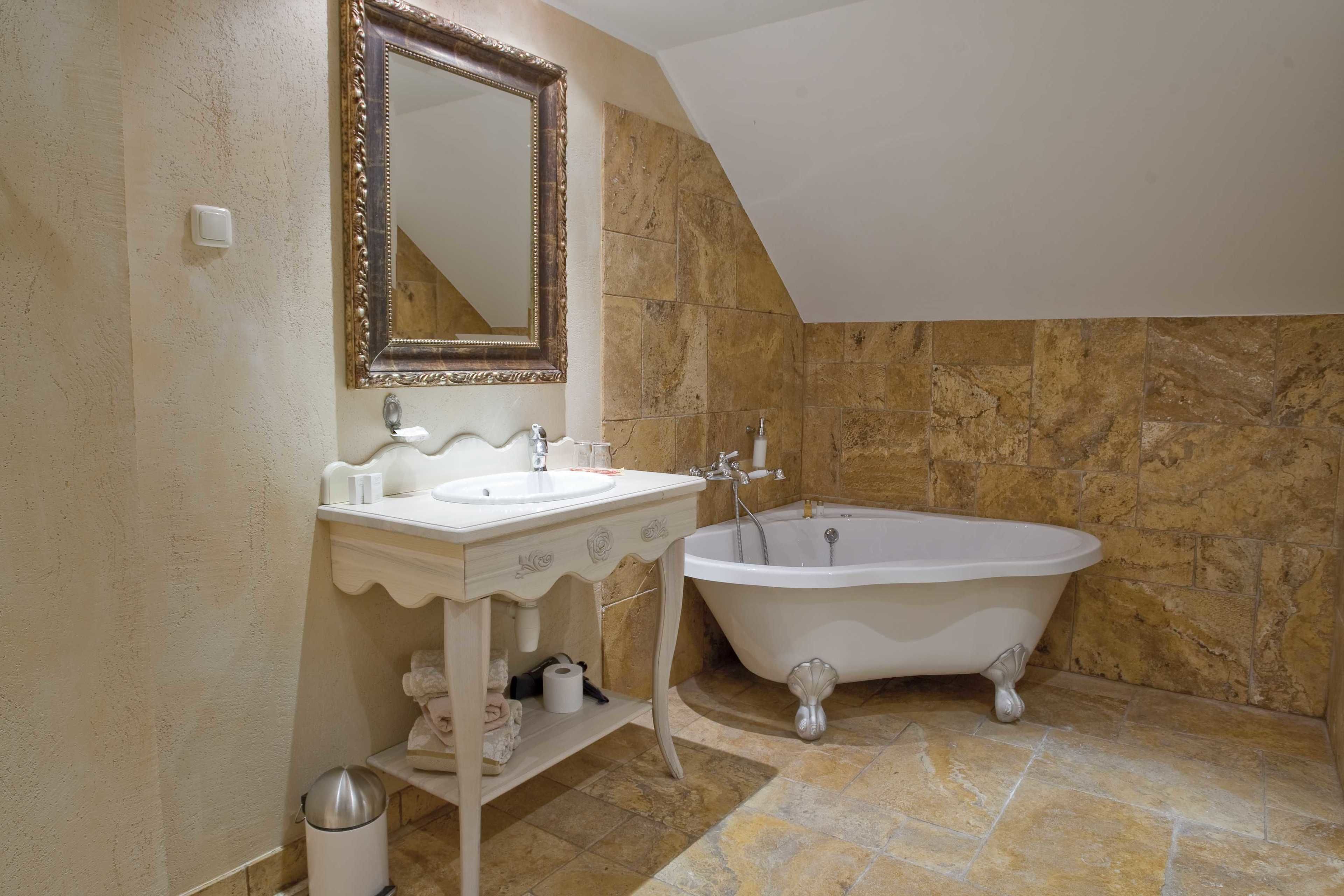 A bathroom with a white vanity, a large mirror, a bathtub, and stone-tiled walls.