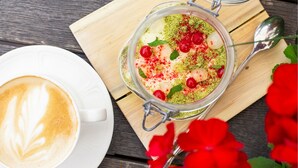 A dessert in a glass jar with cherries and mint leaves, a cup of coffee with latte art, and red flowers on a wooden table. - Grand Rose SPA Hotel (Kuressaare)