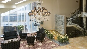 Un amplio vestíbulo con candelabro, sillas tapizadas en negro, alfombra estampada y una escalera de piedra.