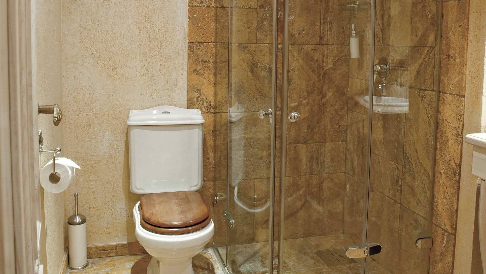 A bathroom with a toilet, a glass shower enclosure, and a marble-tiled wall.
