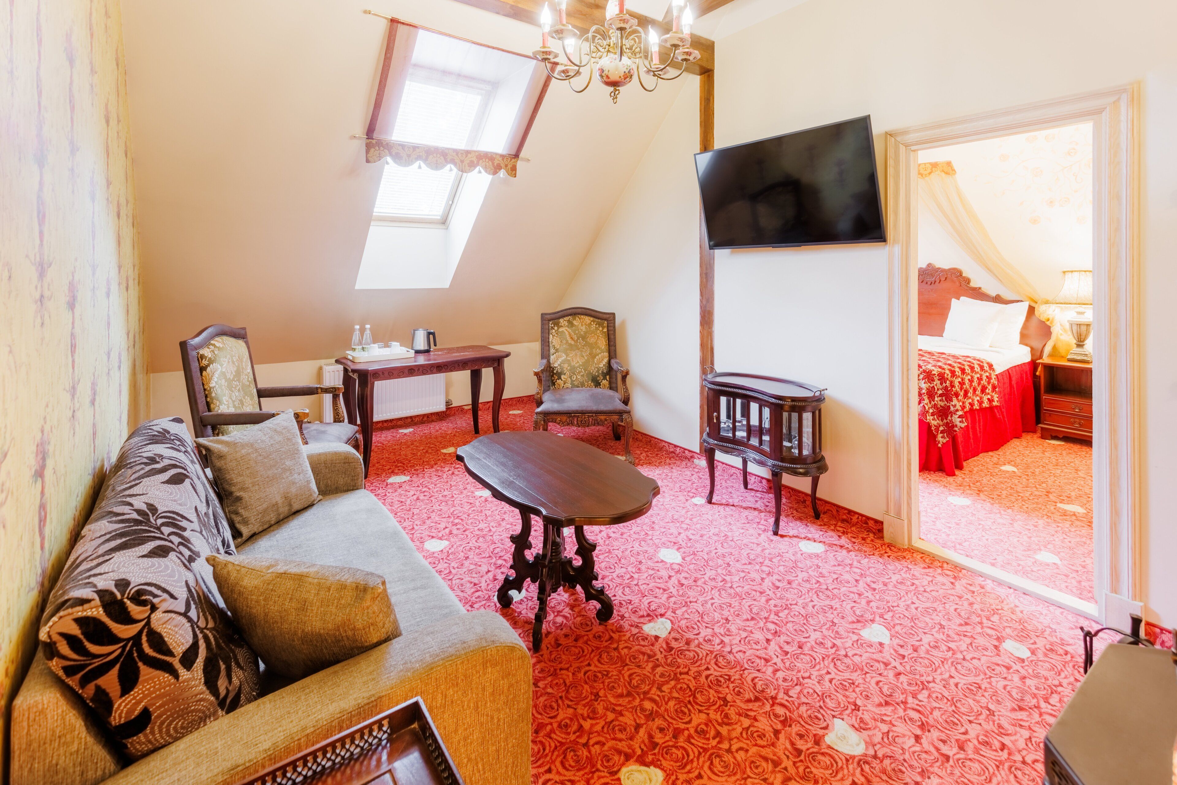 Una habitación con sofá, mesa, silla, televisor y cama con colcha roja.