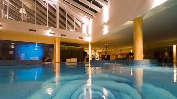 Una piscina interior con agua cristalina, un techo con tragaluces y un diseño arquitectónico moderno.
