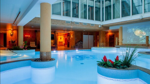 A spacious indoor swimming pool with a central column, surrounded by seating areas and a large mural. - Grand Rose SPA Hotel (Kuressaare)