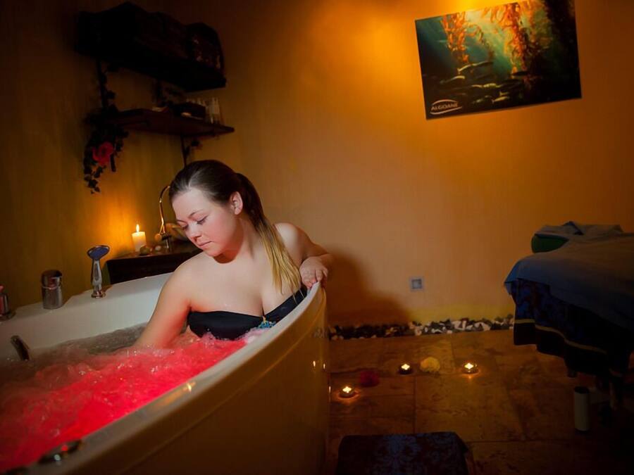 A woman in a bathtub with red water, surrounded by candles and a painting on the wall.