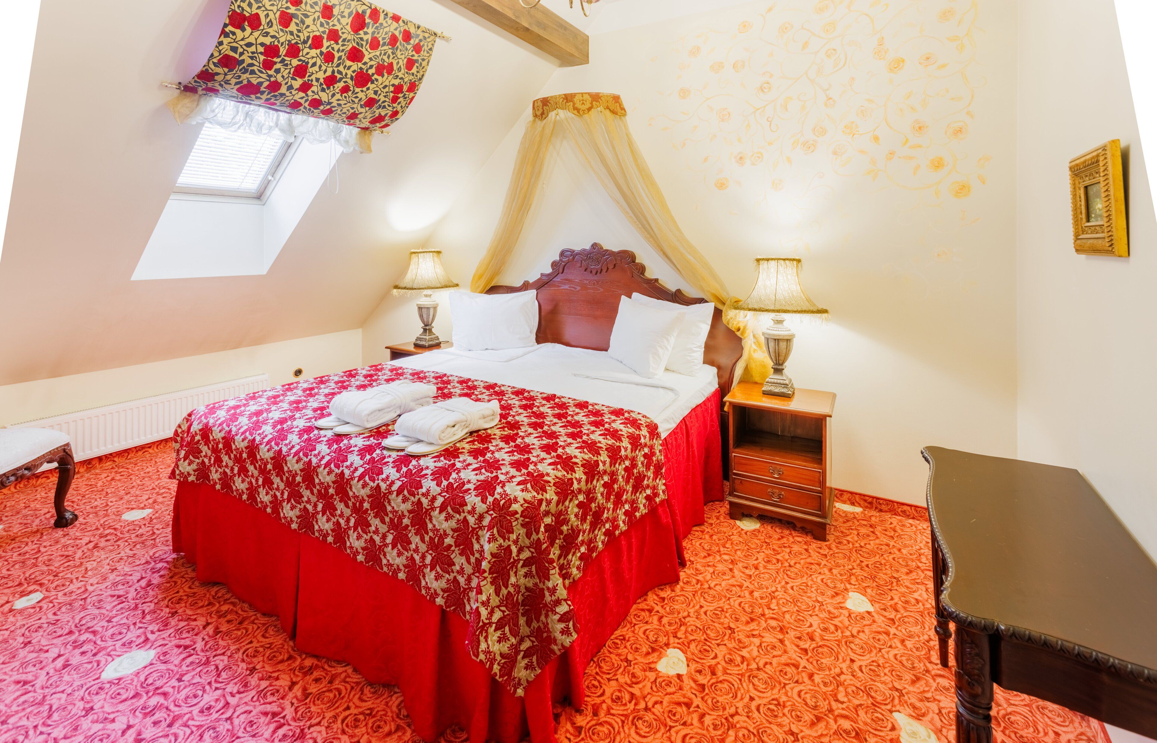 Un dormitorio con cama con dosel, dos mesitas de noche con lámparas, un banco de madera, una pequeña mesa y una ventana con un valance decorativo.