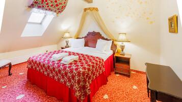 Un dormitorio con cama con dosel, dos mesitas de noche con lámparas, un banco de madera, una pequeña mesa y una ventana con un valance decorativo.