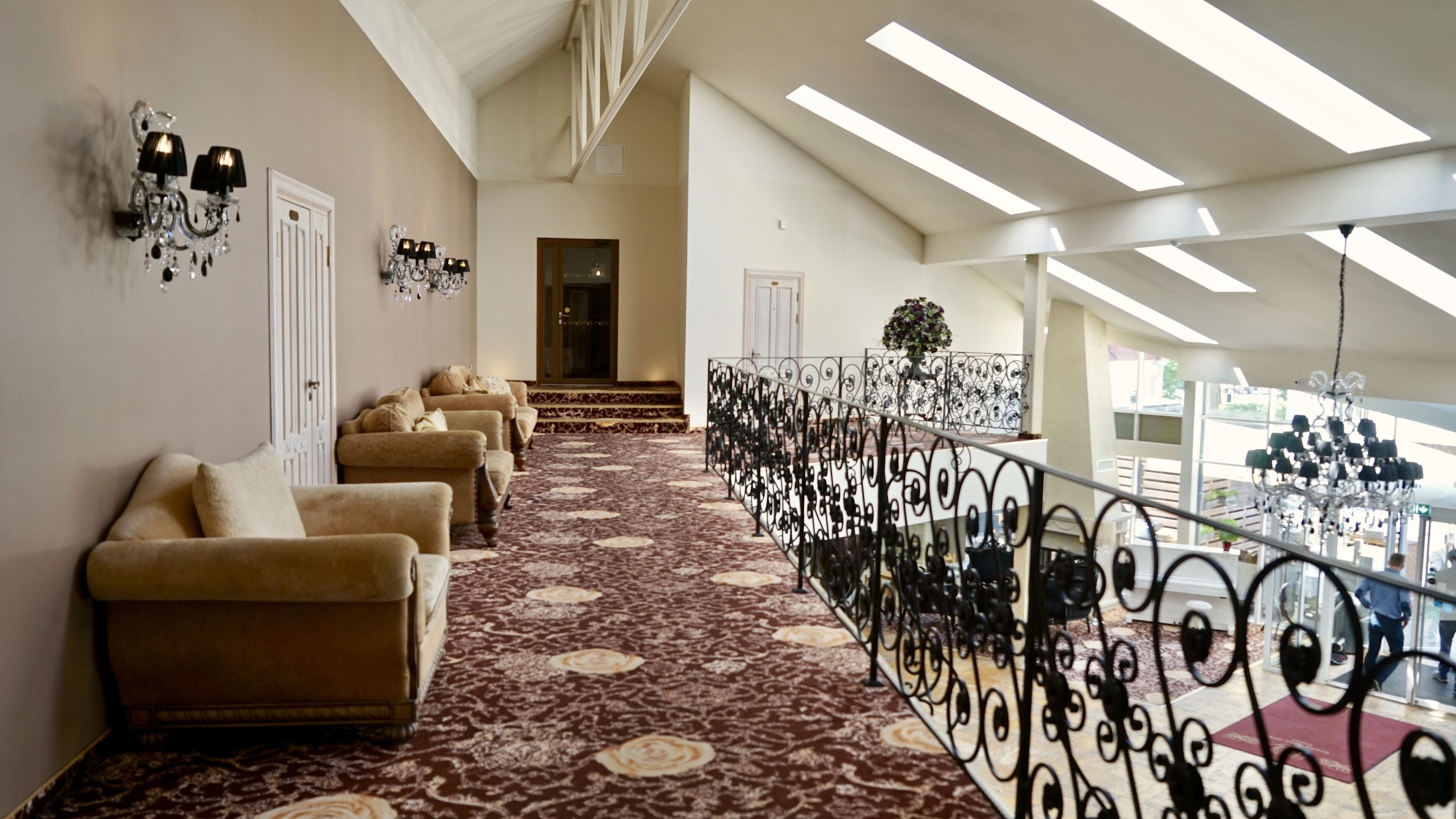 Un hall d’hôtel avec un tapis à motifs, des canapés, des lustres et un balcon doté d’une balustrade.