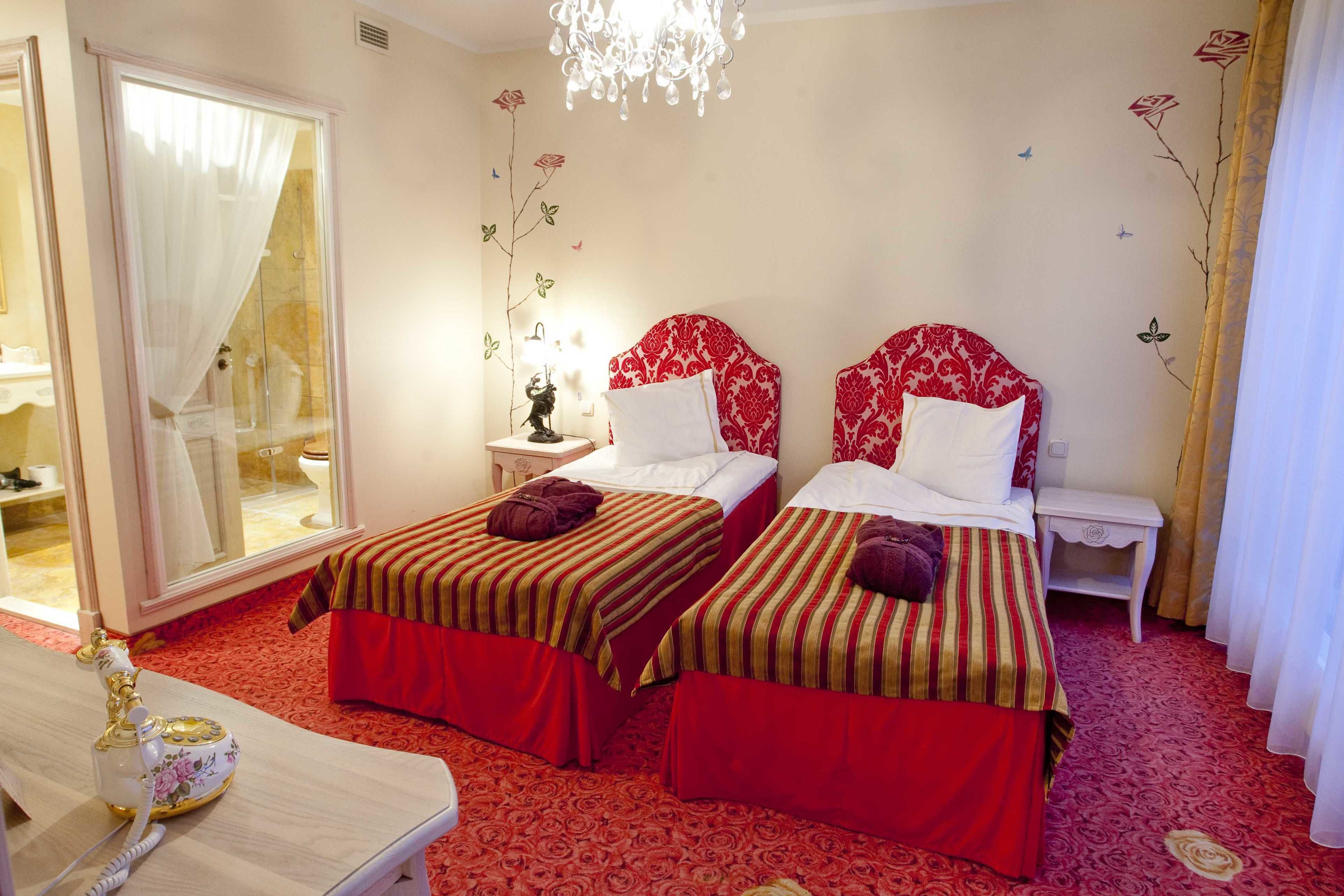Habitación de hotel con dos camas, un rincón de descanso, baño con puerta de vidrio y candelabro.