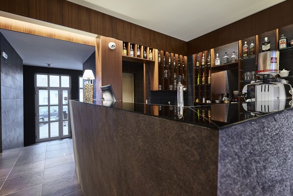 A modern bar area with a polished granite countertop, a coffee machine, and a variety of liquor bottles on shelves.