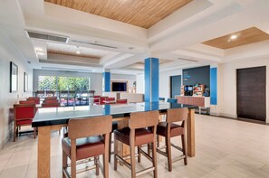 A spacious dining area with a long table and multiple chairs, a coffee station, and a large window providing a view of the outdoors.