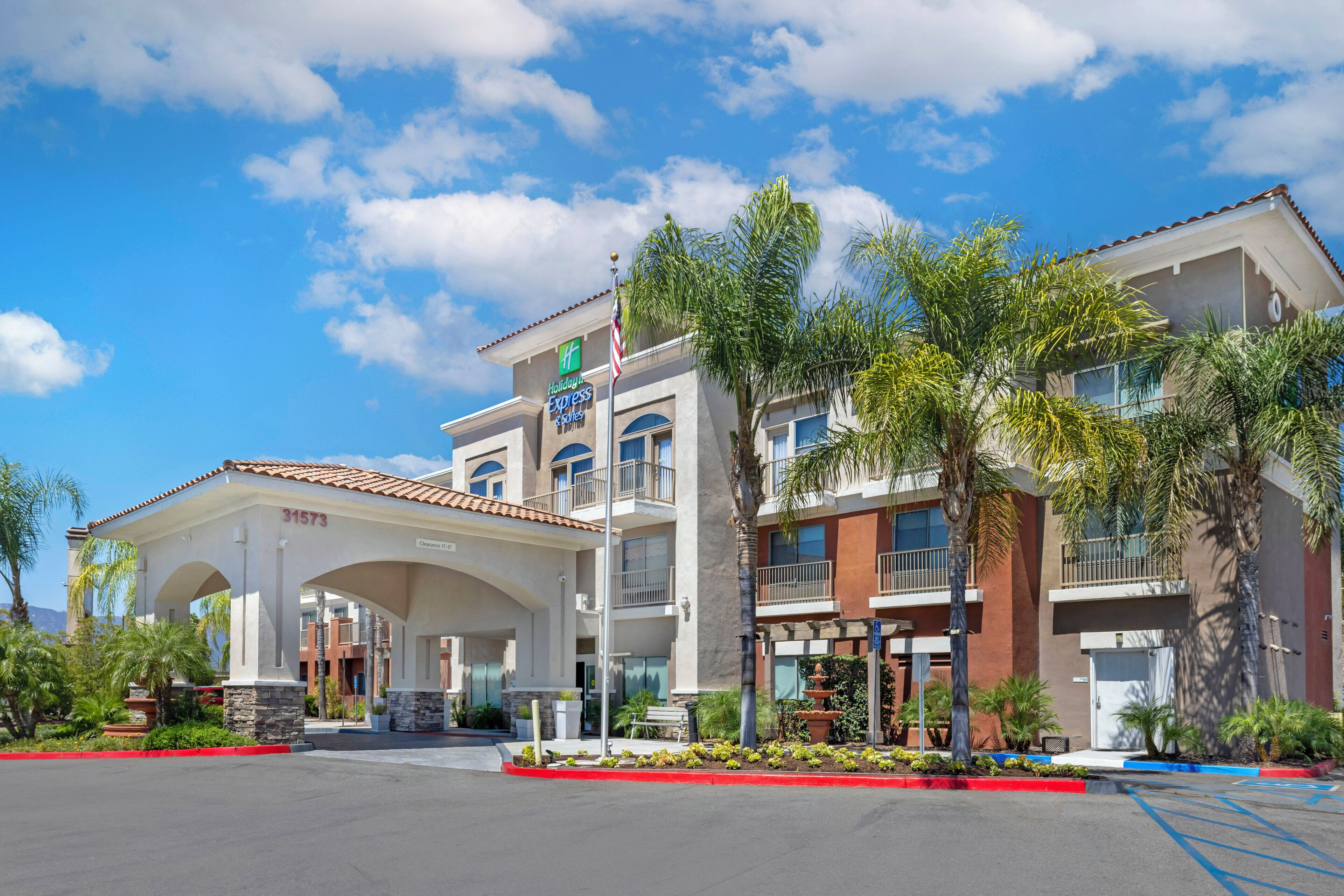 A Holiday Inn Express & Suites hotel with a clear sky, palm trees, and a parking lot.