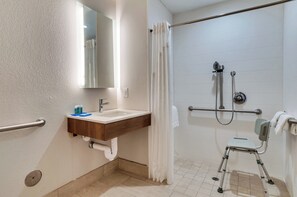 A bathroom with a shower, a sink, and a wheelchair-accessible bench.