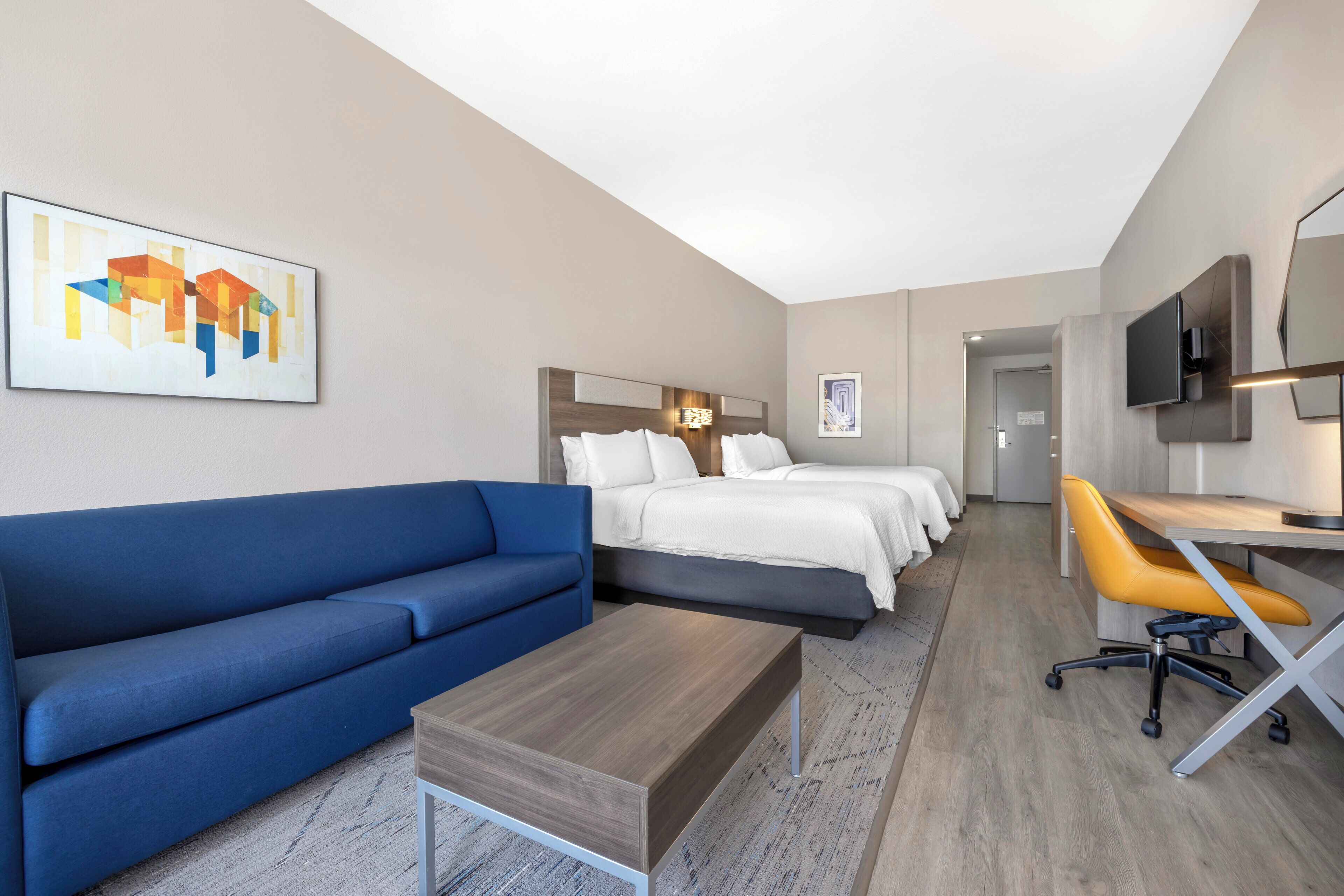 Une chambre d’hôtel avec un canapé bleu, une table basse en bois, un bureau avec une chaise et un lit recouvert de draps blancs.