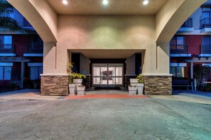 A building entrance with a stone facade, a glass door, and potted plants.