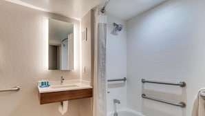 A bathroom with a sink, mirror, shower, and grab bars.