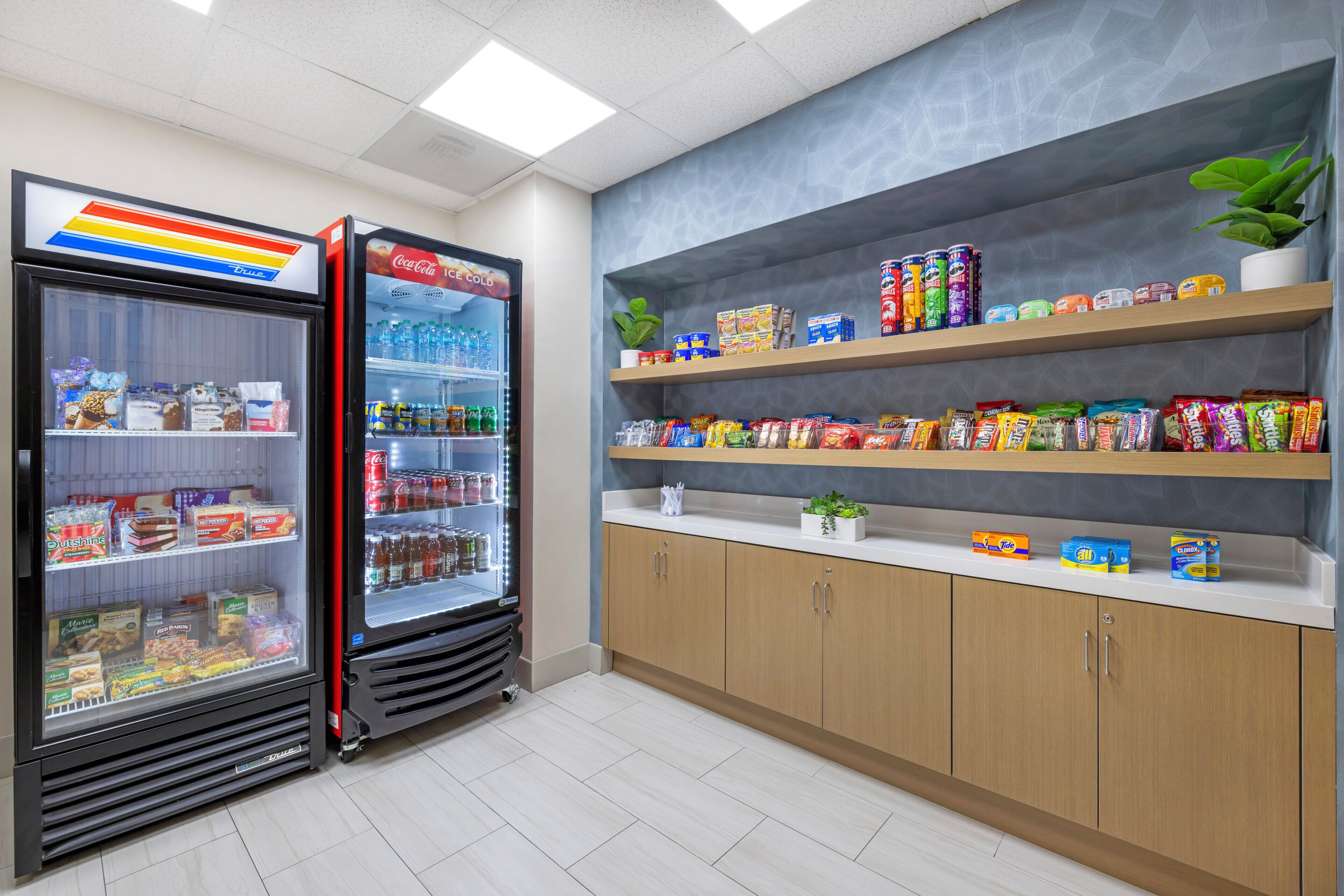 Un espace de vente proposant une variété de collations et de boissons, notamment un réfrigérateur à boissons Coca-Cola et un congélateur contenant divers produits.