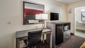 A hotel room with a desk, chair, TV, refrigerator, microwave, and a patterned carpet. - Econo Lodge Thomasville (Thomasville)