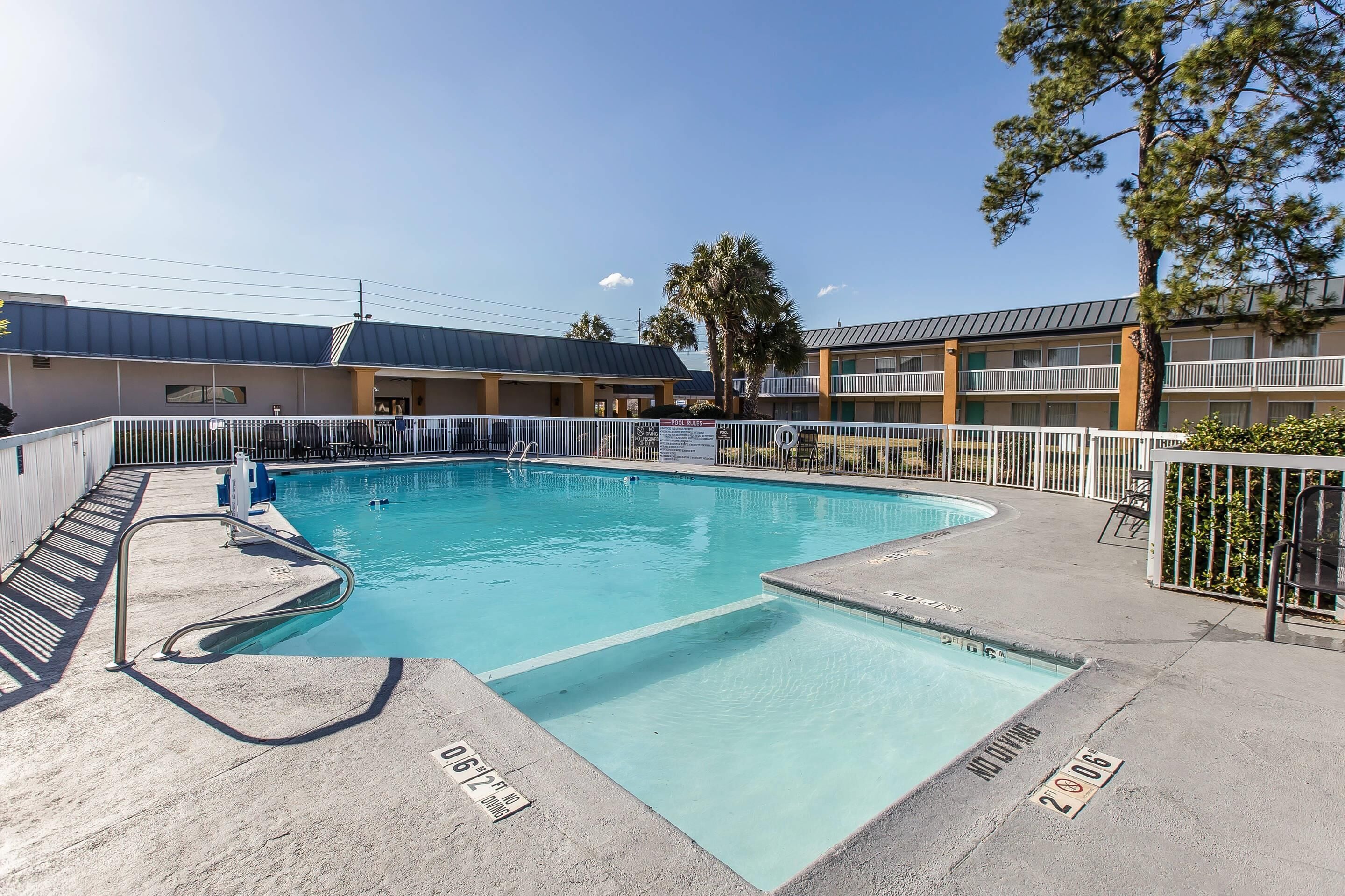 A swimming pool with a metal ladder, a concrete deck, and a building with multiple balconies in the background.
