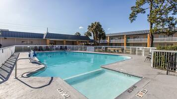 A swimming pool with a metal ladder, a concrete deck, and a building with multiple balconies in the background.