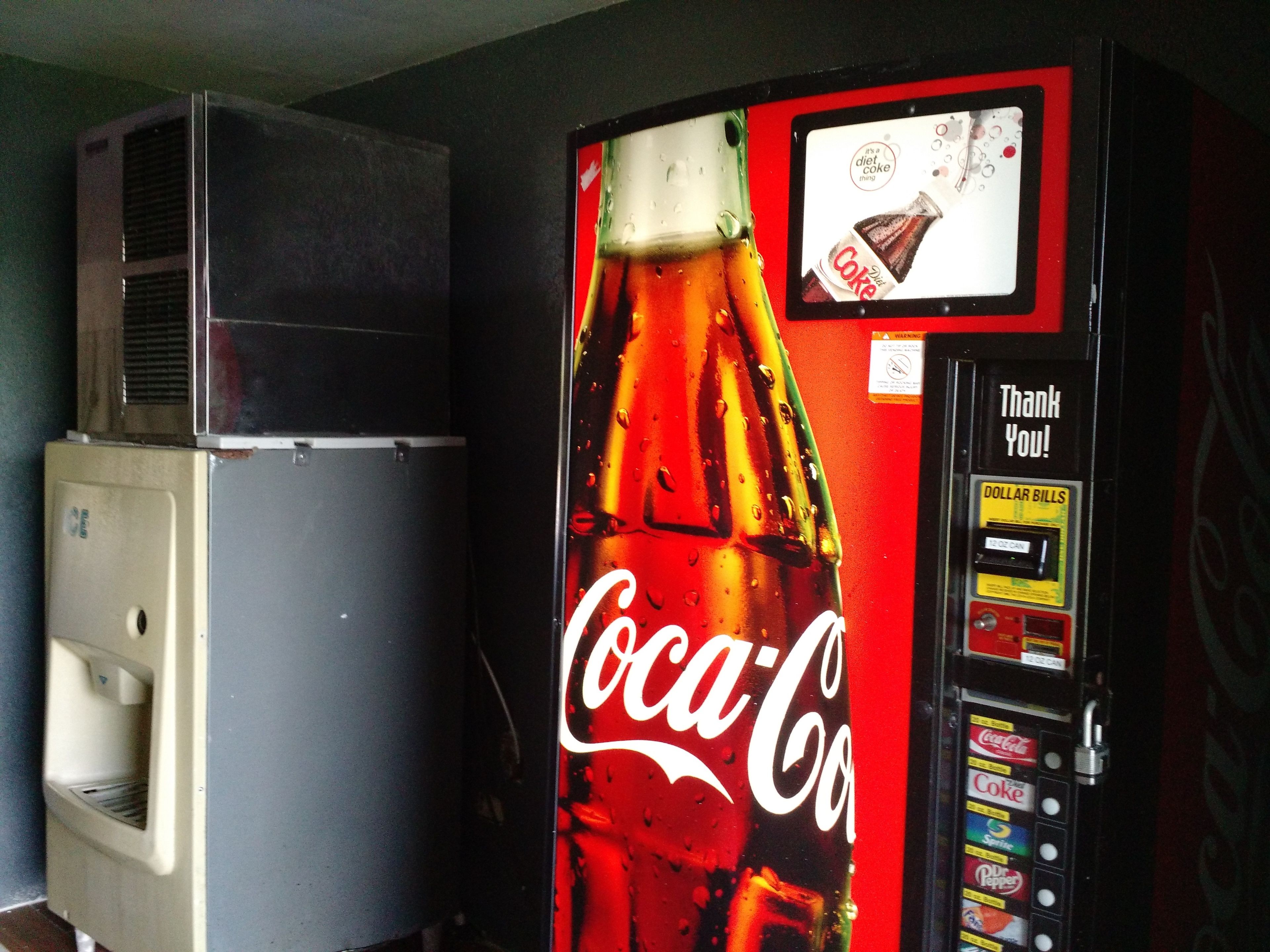 A Coca-Cola vending machine with a payment slot and a warning label.