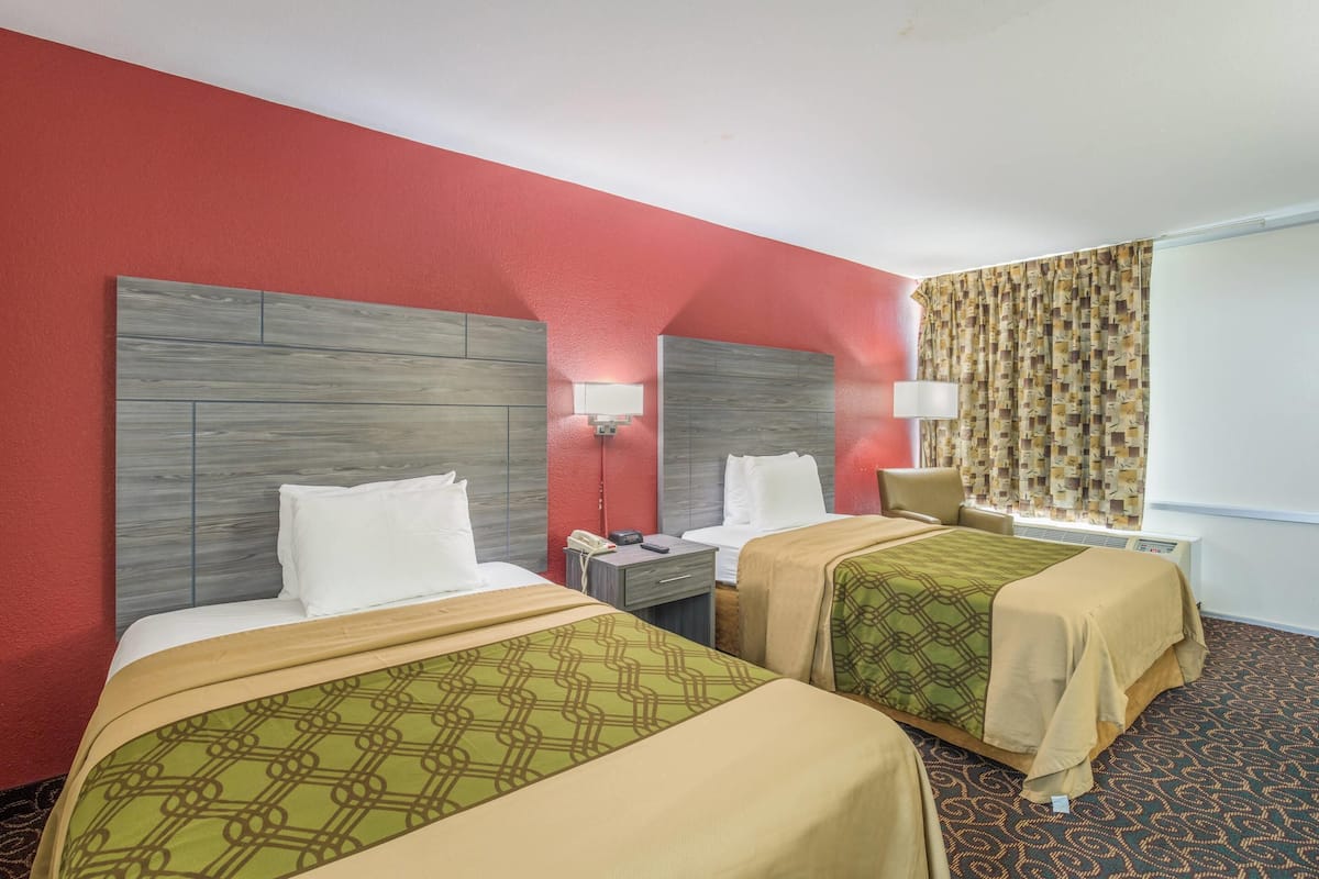 Hotelkamer met twee bedden, een bureau, een stoel, een raam met gordijnen en een airconditioner aan de muur.