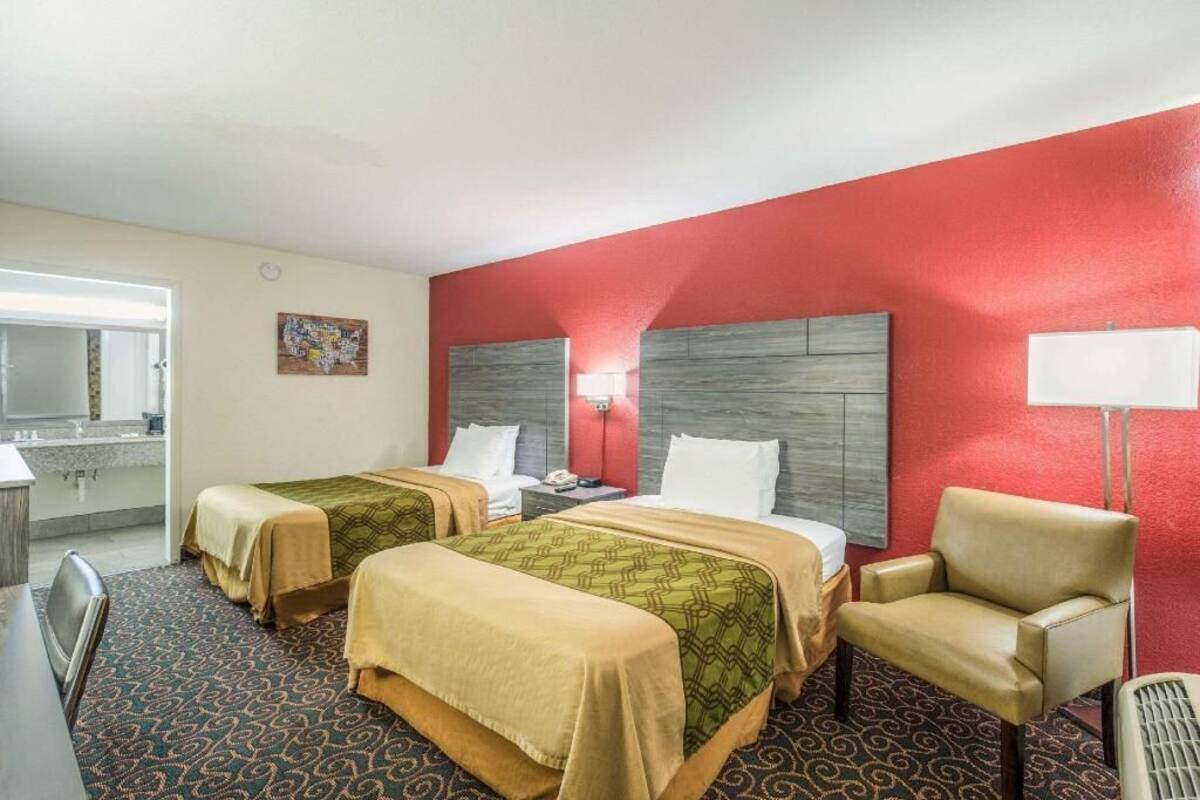 Een hotelkamer met twee bedden, een bureau, een stoel, een lamp en een zichtbare badkamer door een open deur.